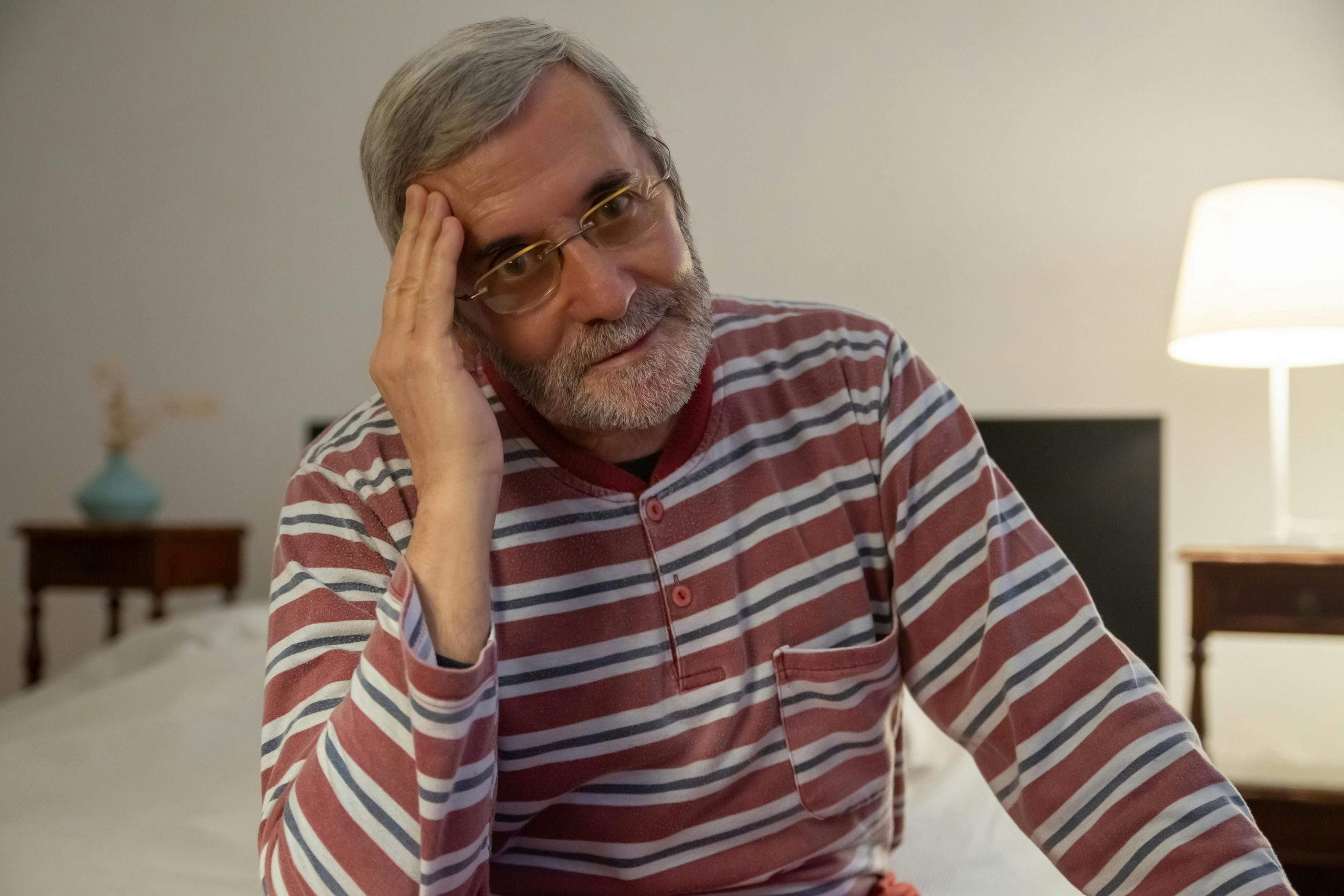 Senior man in striped pajamas resting indoors with a contemplative look.